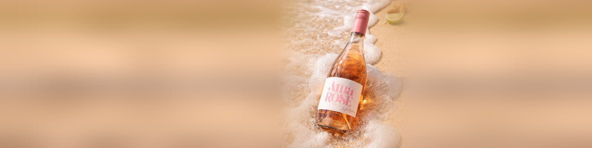 Botella de Ama Rose en la espuma de la orilla, con la arena y el mar de fondo